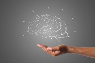 Dibujo de un cerebro con puntos y líneas luminosas sobre una mano abierta, en fondo gris