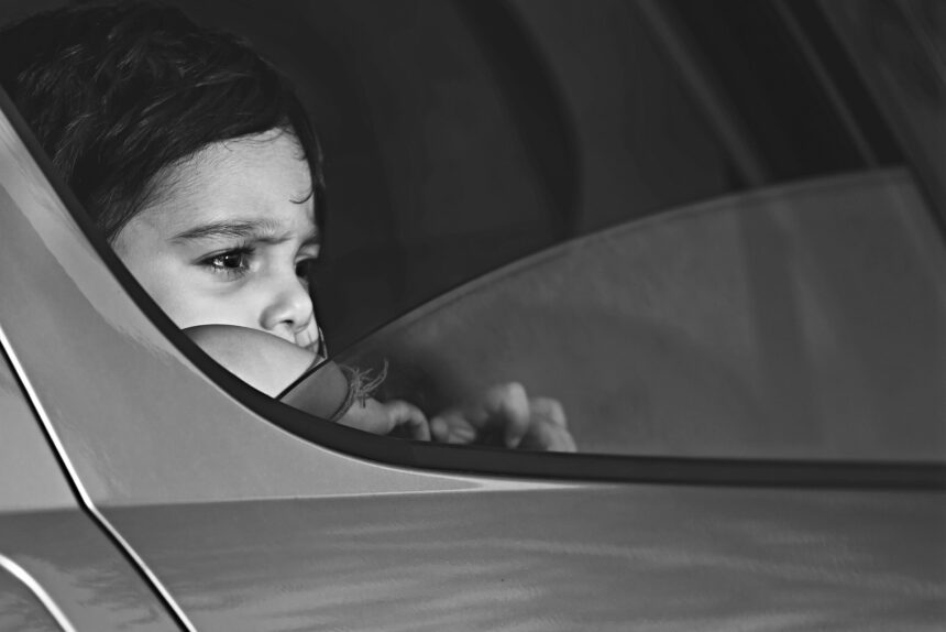Primer plano en blanco y negro de un niño que mira con gesto serio por la ventanilla de un coche