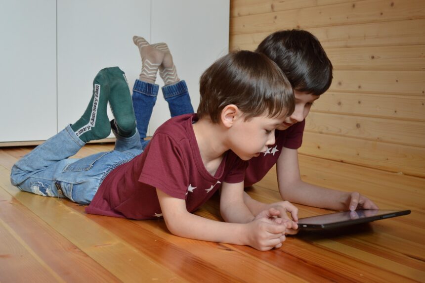 Dos niños tumbados en el suelo miran juntos la pantalla de una tableta