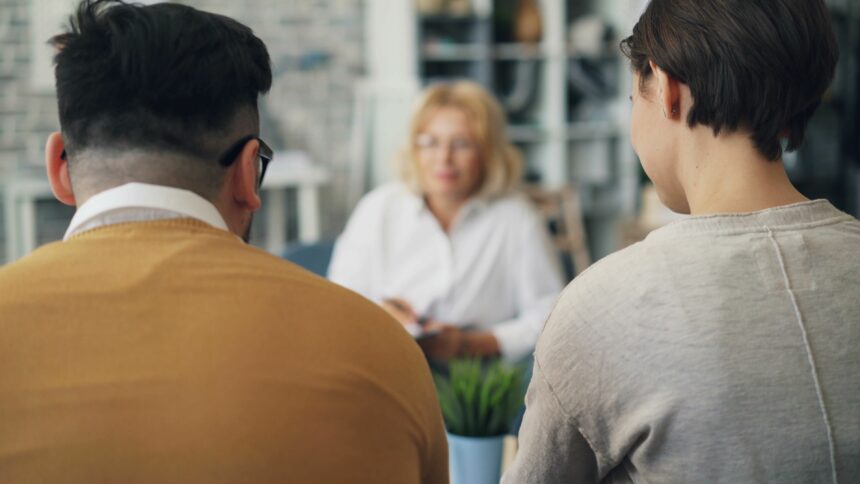 Dos personas de espaldas conversan con una profesional en una consulta